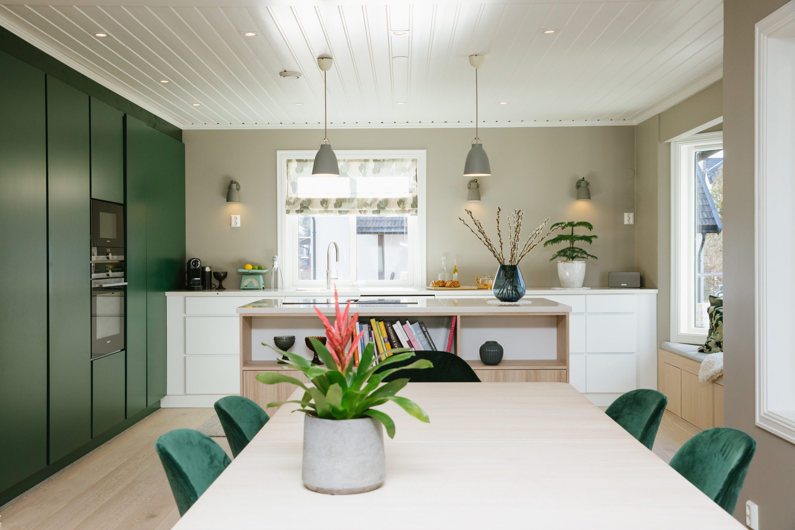 Romslig kjøkken med grønne høyskap, kjøkkenøy og spisestue med grønne stoler